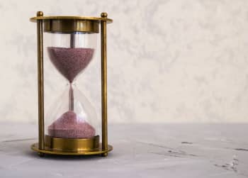 A traditional hourglass with pink sand, symbolizing time and patience on a textured surface.